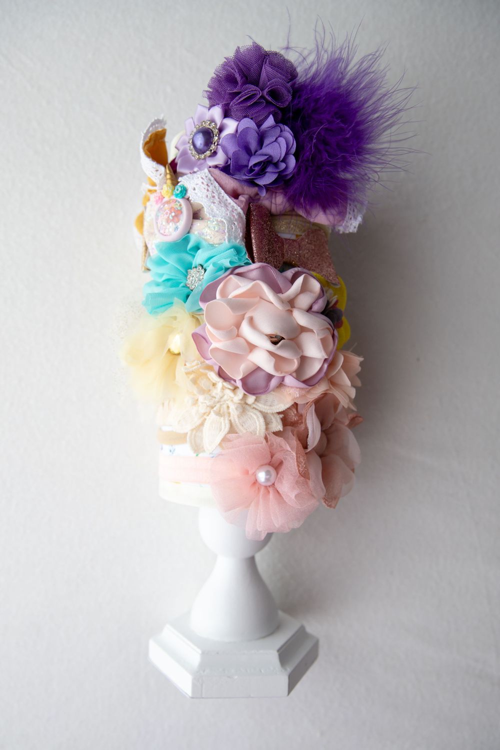 Ornate floral headpiece with purple feathers, flowers, and pearls displayed on a white bust stand.