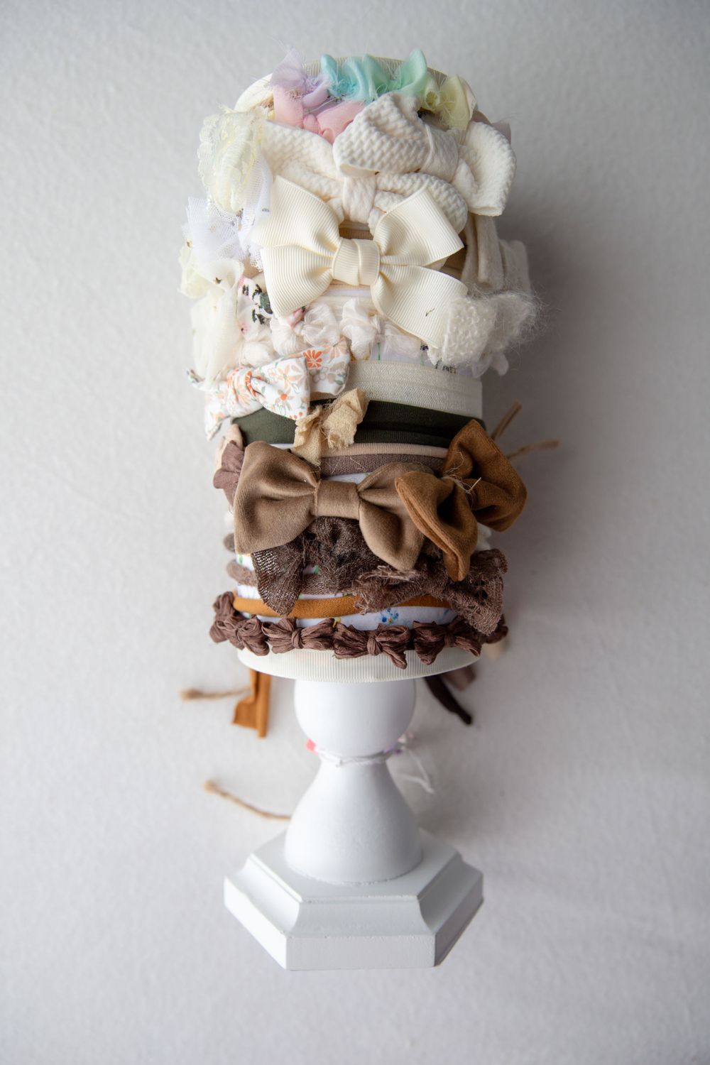 White pedestal displaying stacked neutral brown and cream fabric hair bows and headbands.
