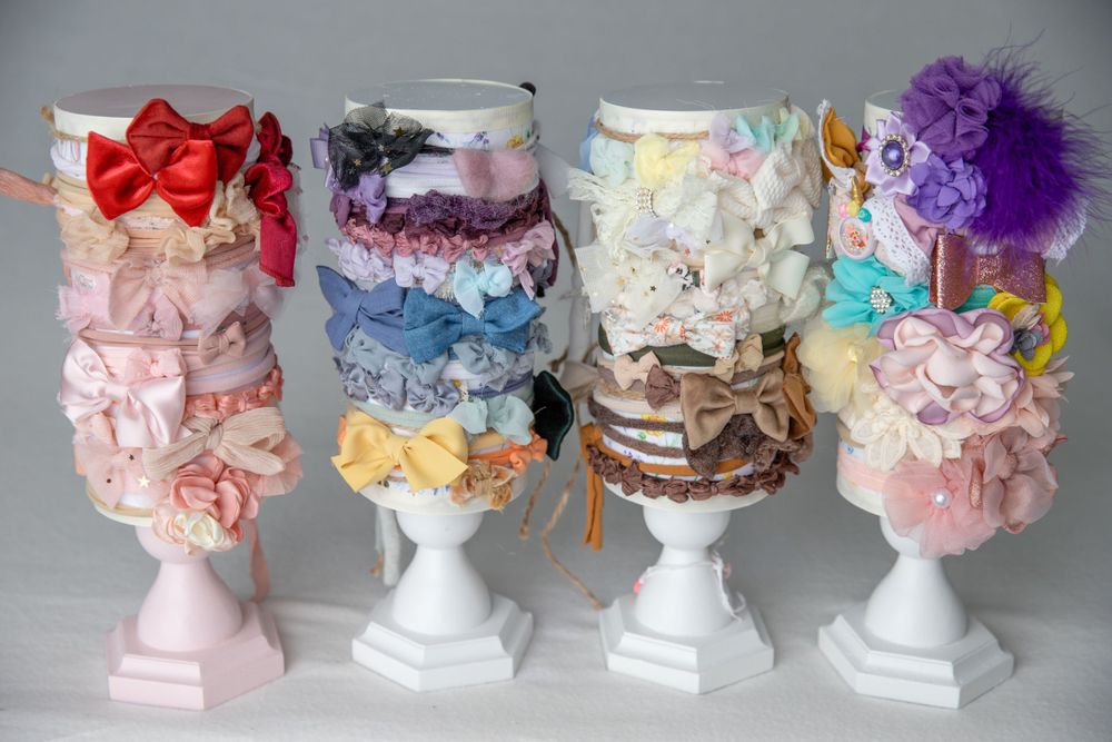 Four white pedestals displaying organized collections of colorful baby hair bows and headbands.