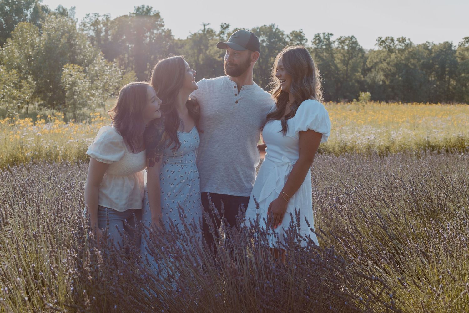A family standing together in a sunlit field of tall grass during golden hour.