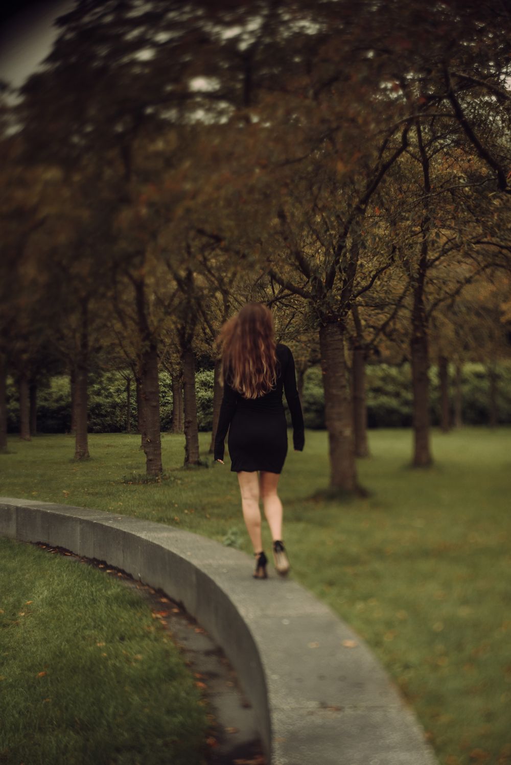 Figure walking along curved path through autumn trees in park.