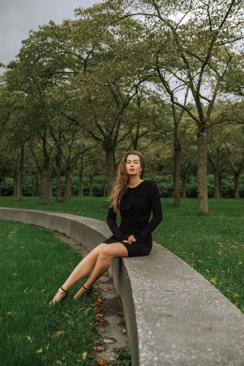 Artistic portrait session on a curved concrete wall in a lush park setting.