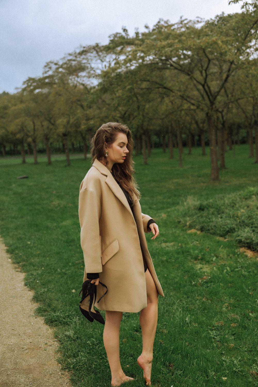 Outdoor fashion photography in an orchard featuring tan coat and black dress styling.