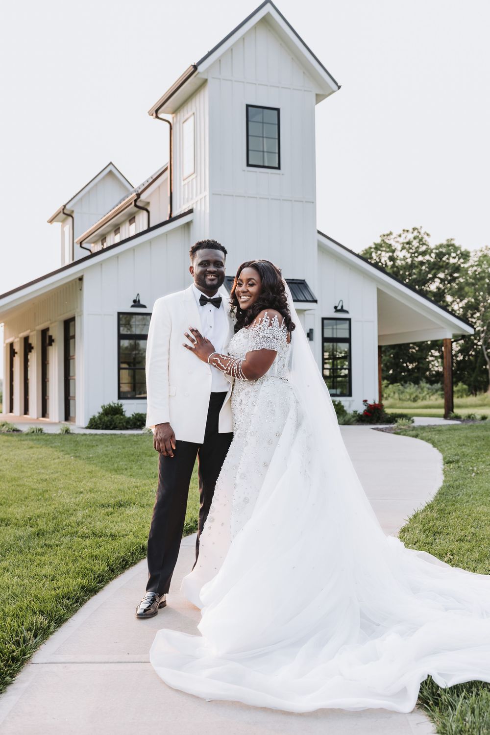A beautiful wedding couple stands outside a modern white church with a tower on a sunny day.
