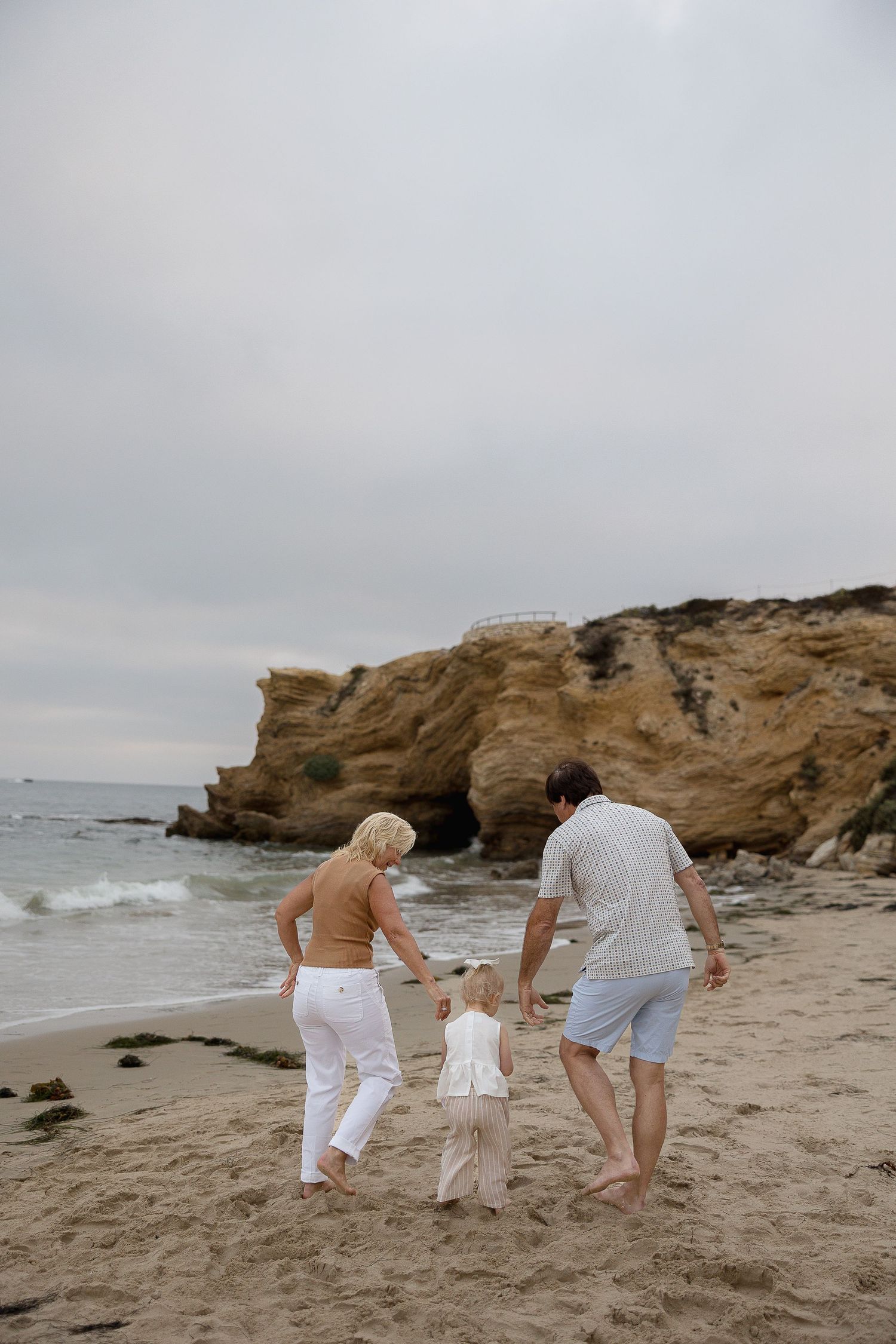Crystal Cove family photos capturing grandparents and granddaughter walking at the beach