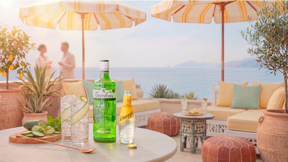 Tanqueray gin bottle displayed on a terrace table with limes and tonic water, overlooking a scenic Mediterranean coastline.