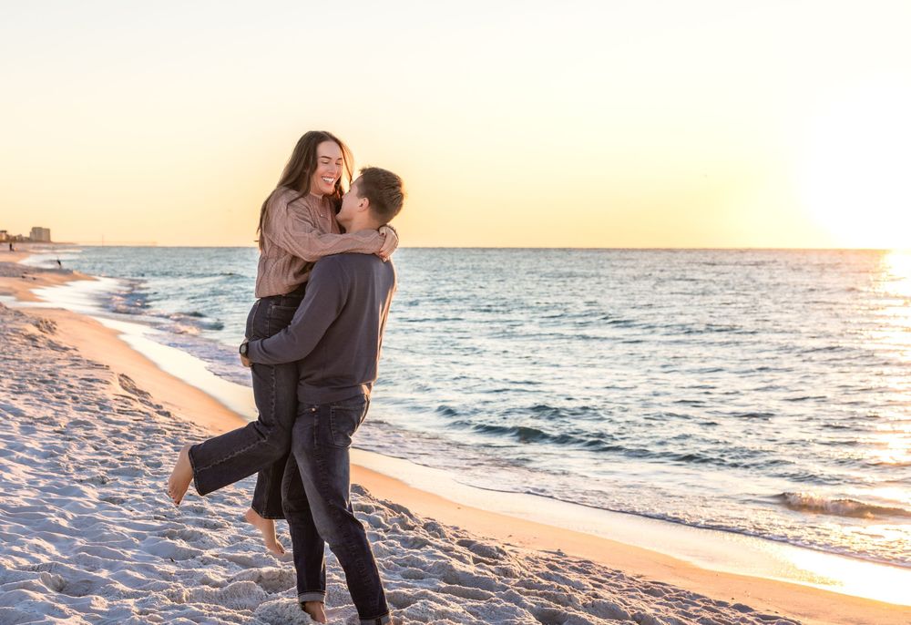 Romantic couple embracing on sandy beach at sunset with ocean waves in the background.