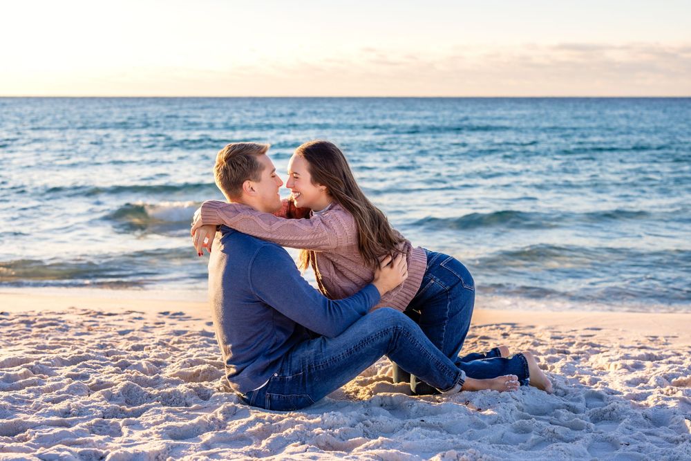 Couple relaxing together on sandy beach at sunset with ocean waves in background.