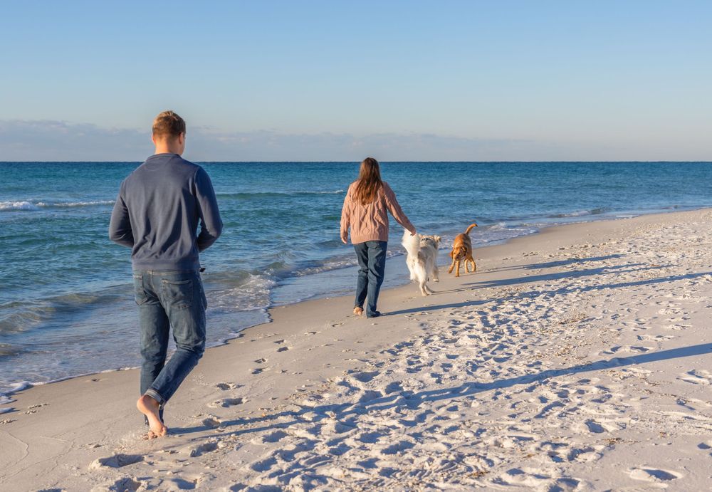 People walking along a pristine white sandy beach with crystal blue ocean waters on a sunny day.