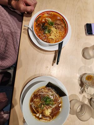 A bowl of steaming hot noodle soup with vegetables and meat in a rich brown broth garnished with fresh herbs.