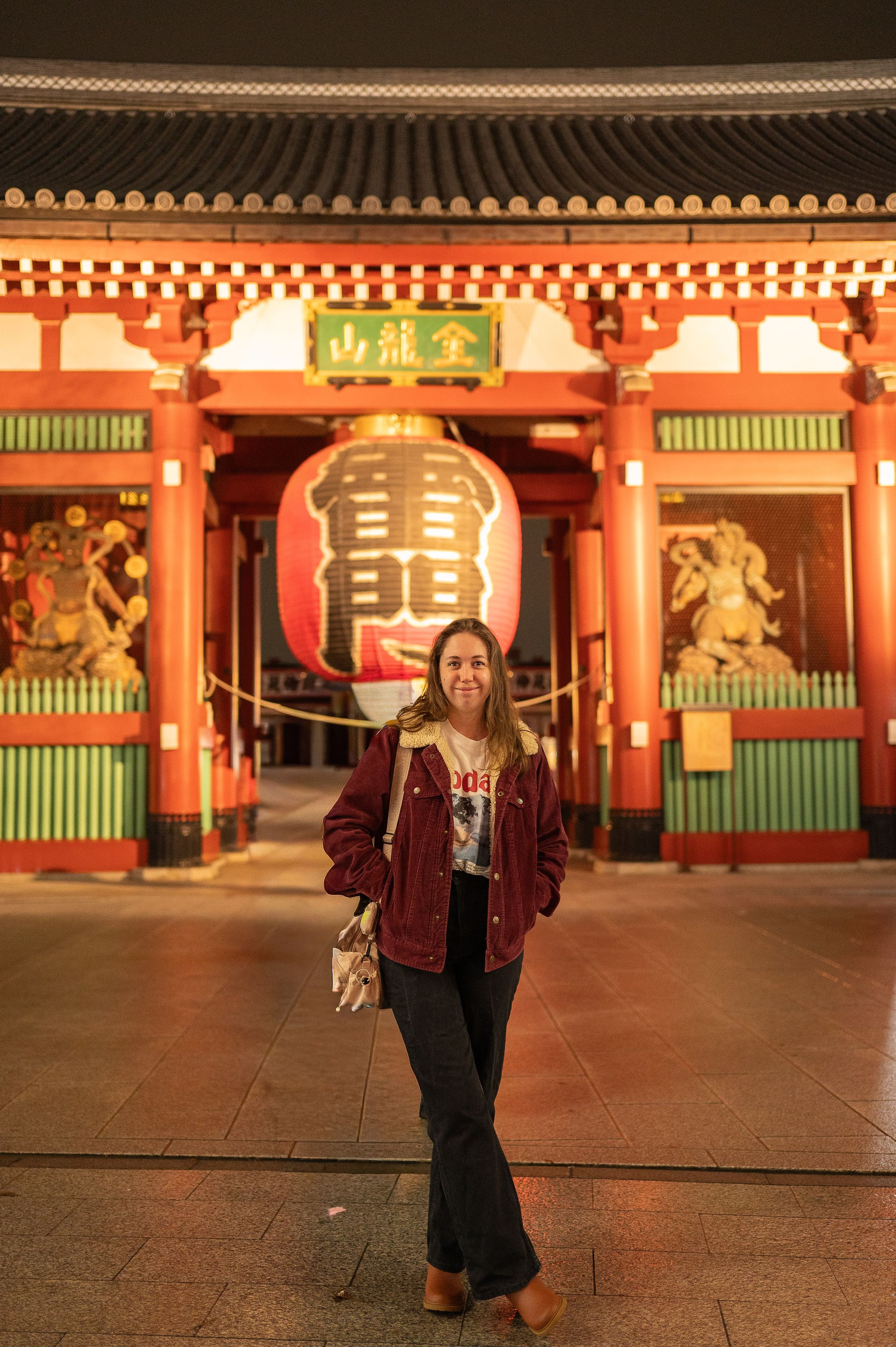 A person in traditional Japanese clothing walks through the illuminated corridors of Sensoji Temple at night.