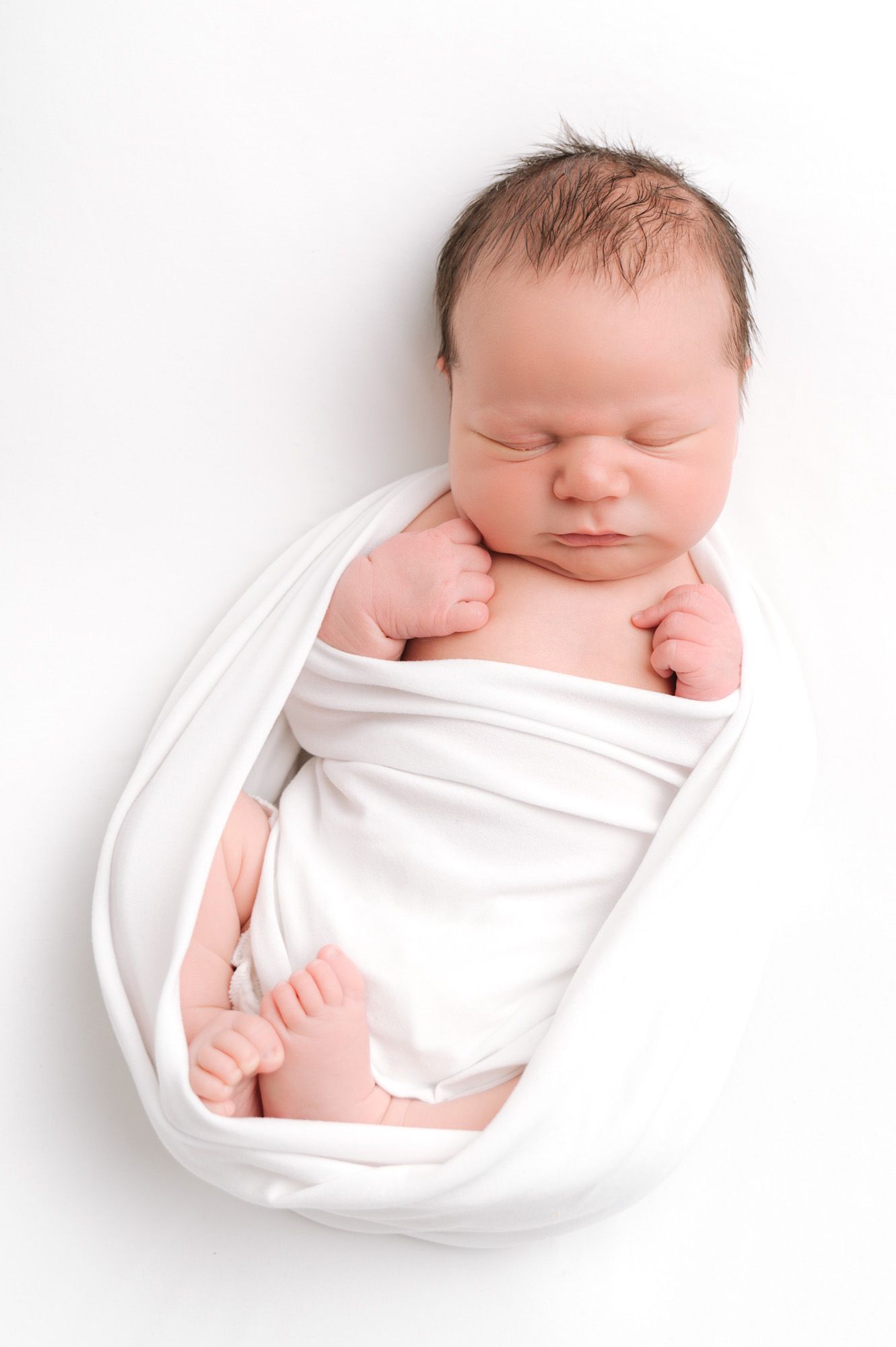 A sleeping newborn baby wrapped in white cloth shown from four different angles on a pure white background.