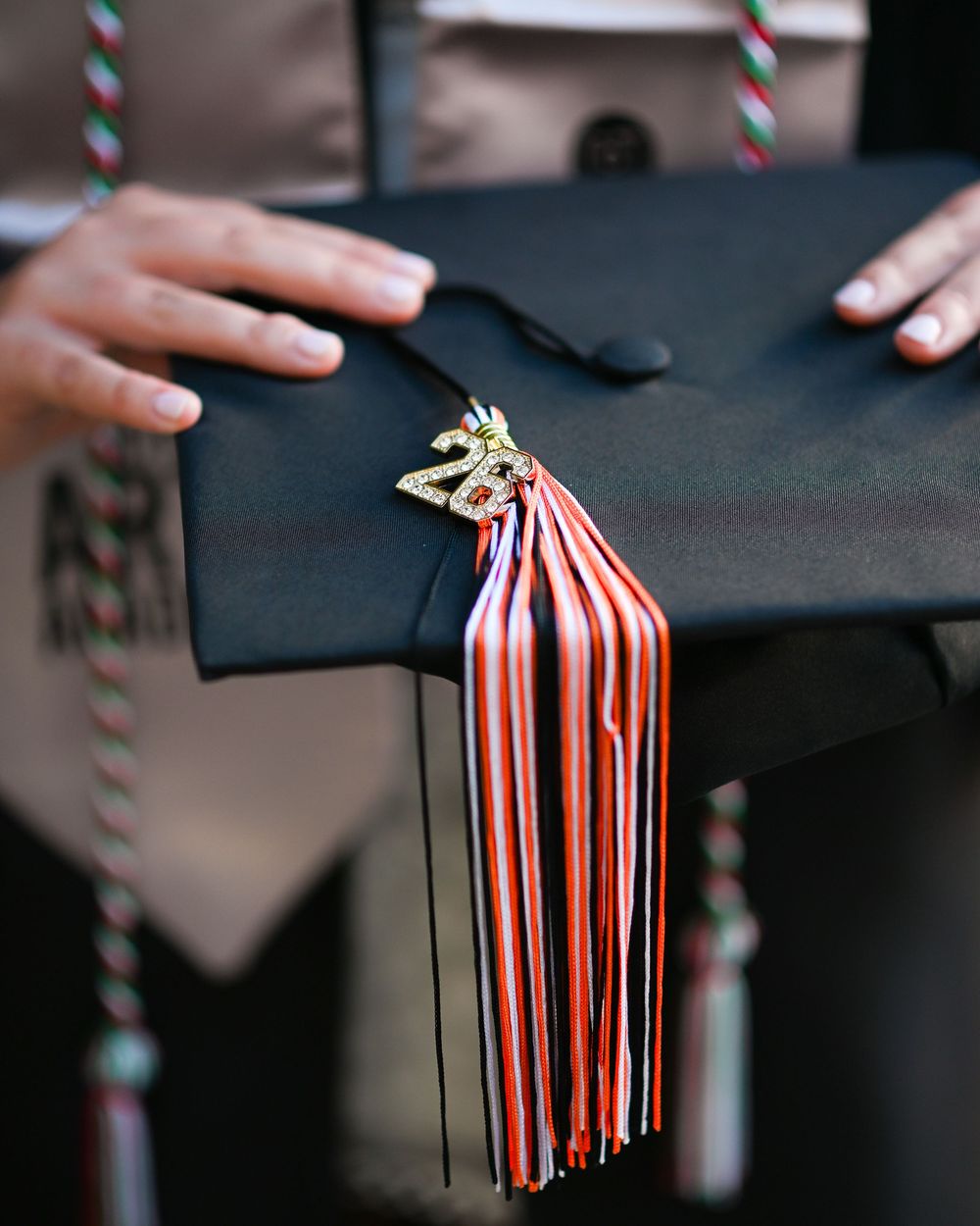 Close-up of a black graduation cap with red and white striped tassel and gold 2023 charm held by graduate.
