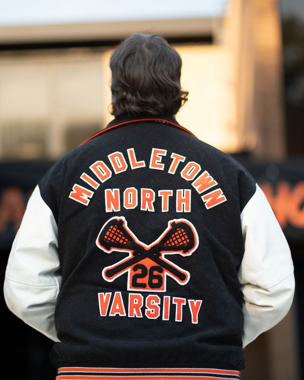 Person wearing a Middletown North Varsity lacrosse letterman jacket with number 26, featuring crossed lacrosse sticks.