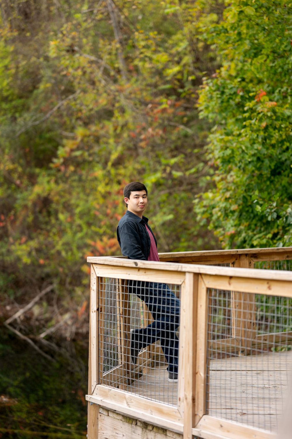Young Asian man standing on elevated wooden deck platform surrounded by vibrant autumn foliage.