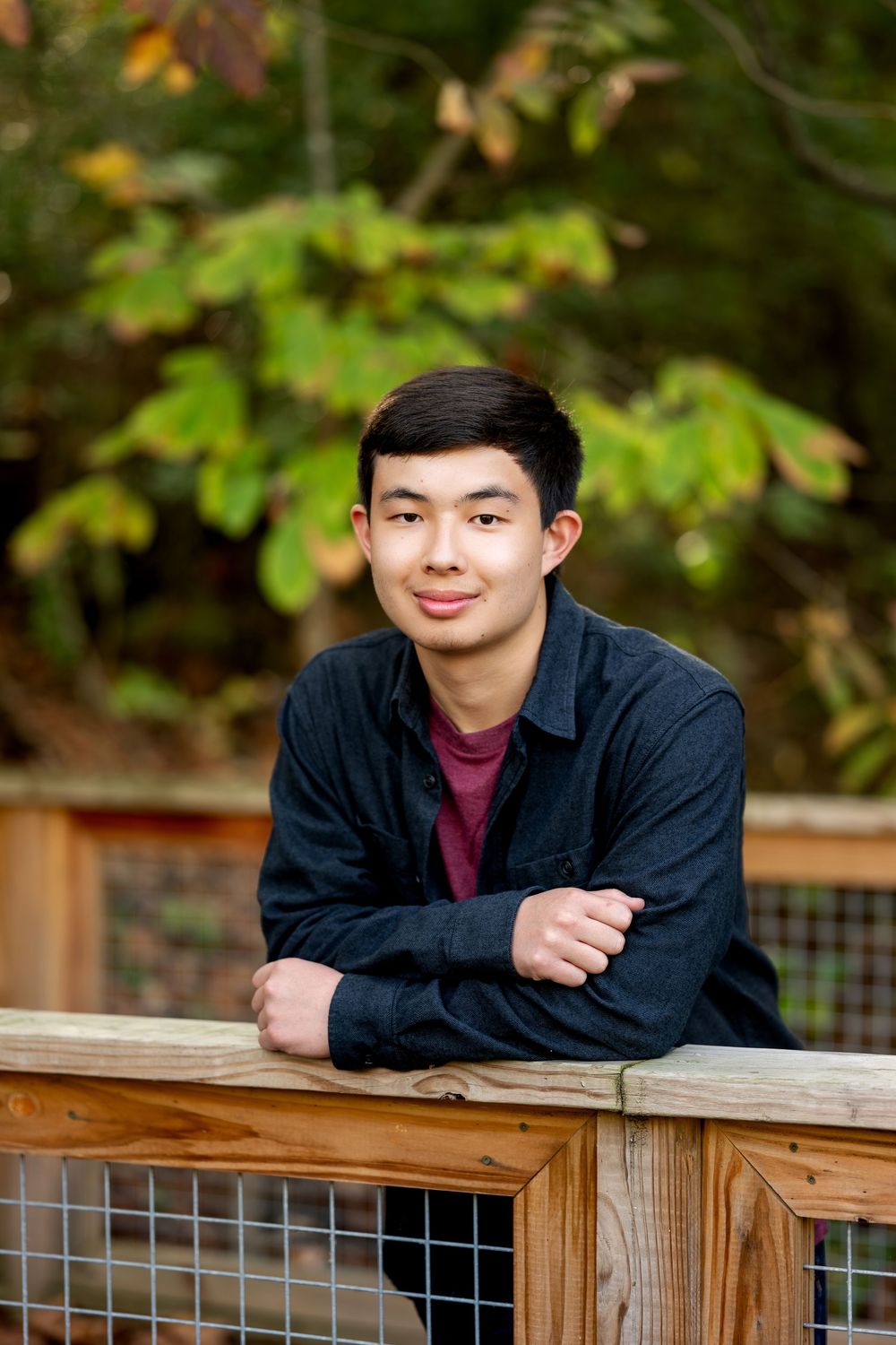 Young Asian man leaning on wooden fence smiling in autumn park.