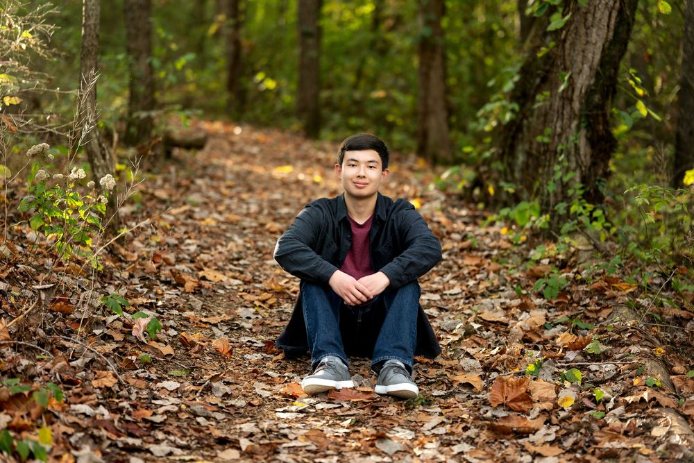 Young man sitting on leaf-covered forest path in autumn woodland.