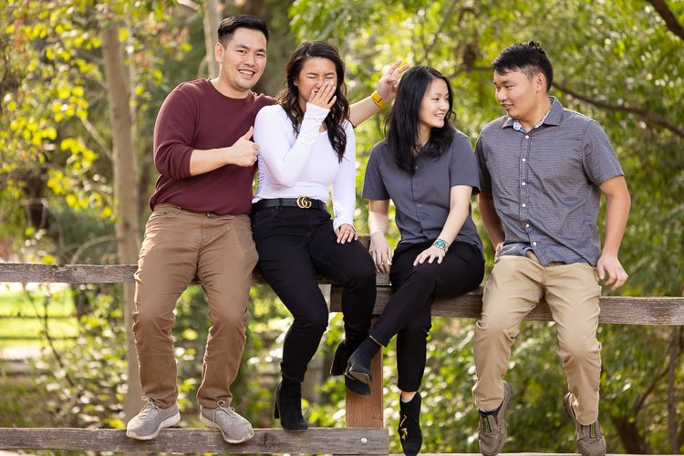 A family of four grown children sit together on a wooden fence in a park with autumn foliage in the Bay Area.