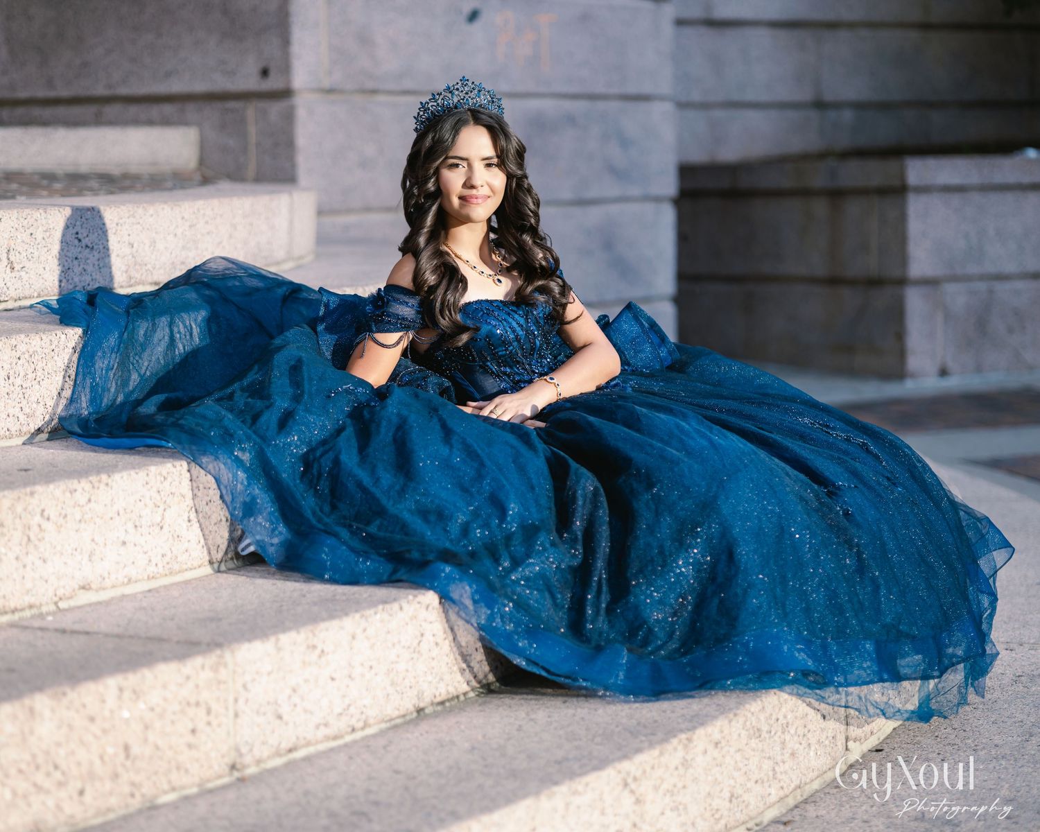 A flowing navy blue tulle gown with off-shoulder design photographed in a dramatic collage against stone architecture.