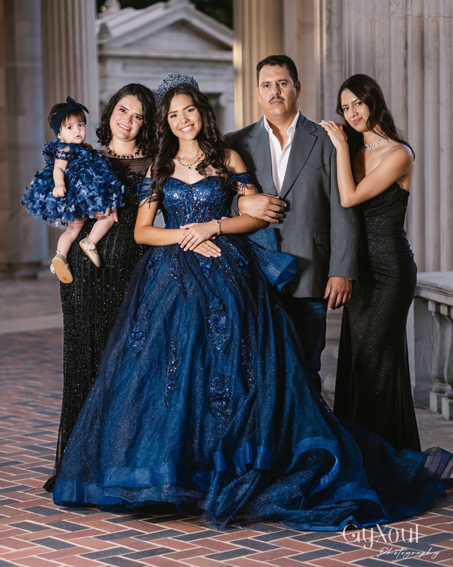 A formal group wearing elegant navy blue gowns and dark suits poses together in an architectural setting.