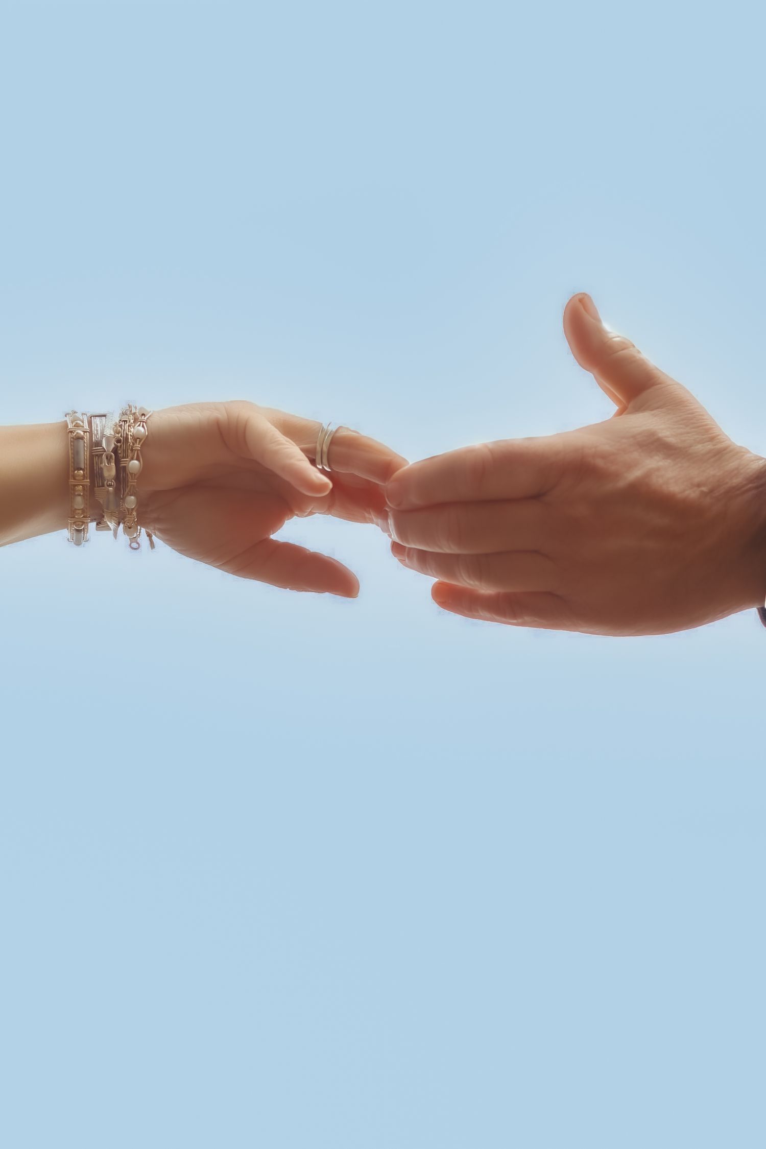 Sequence of hands reaching out to connect against blue sky background.