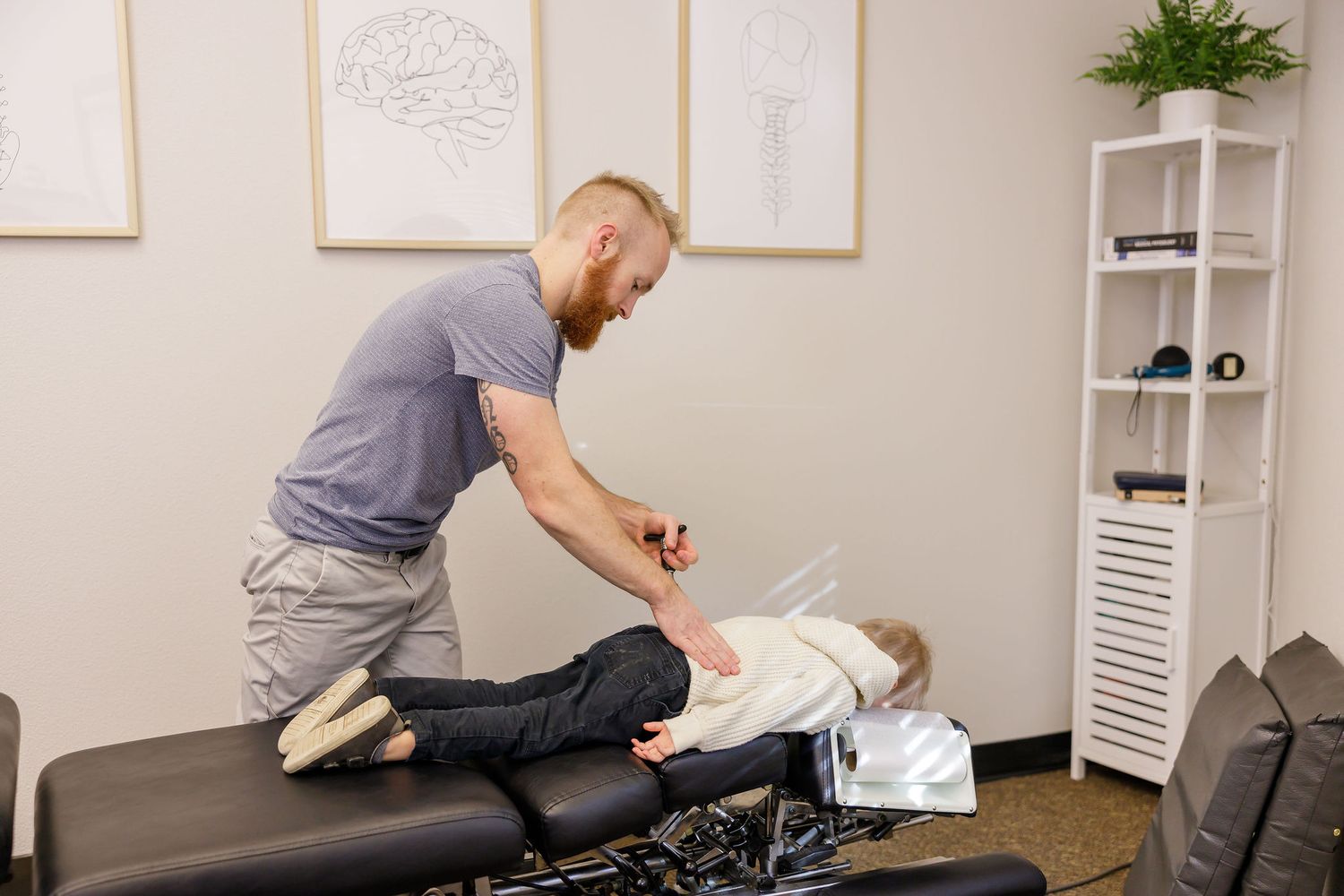 chiropractor branding photo in Sumner, WA wellness health man adjusting little boy using activator while laying face down on treatment table