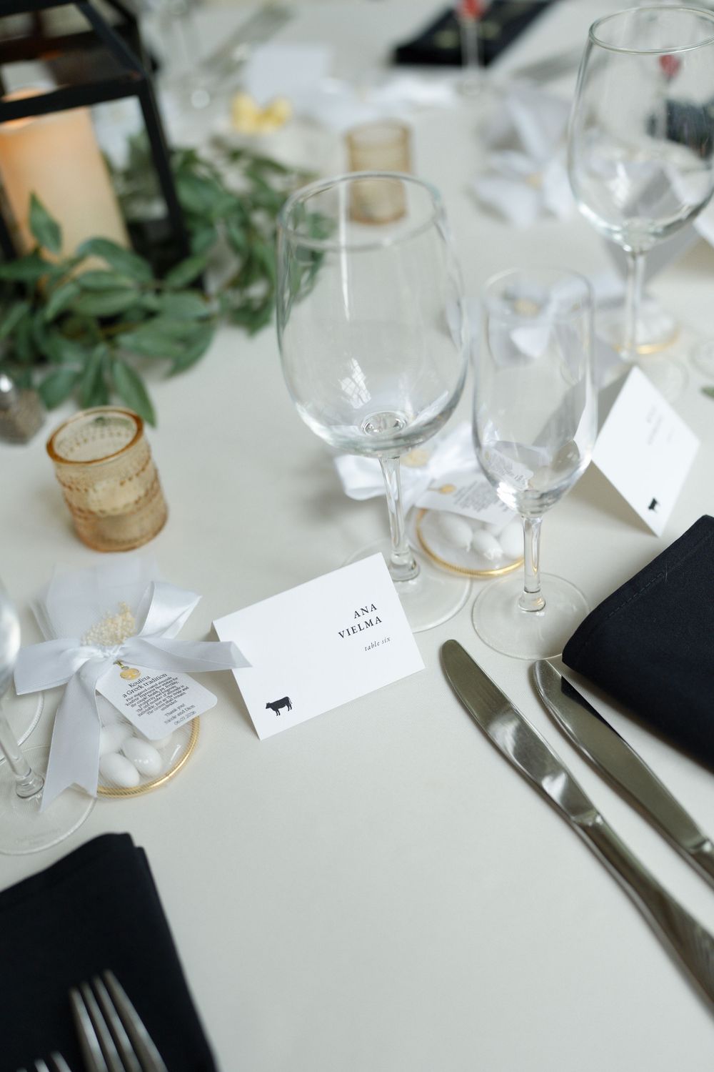 Elegant wedding table setting with crystal glasses, black napkins, place cards, and floral centerpiece.