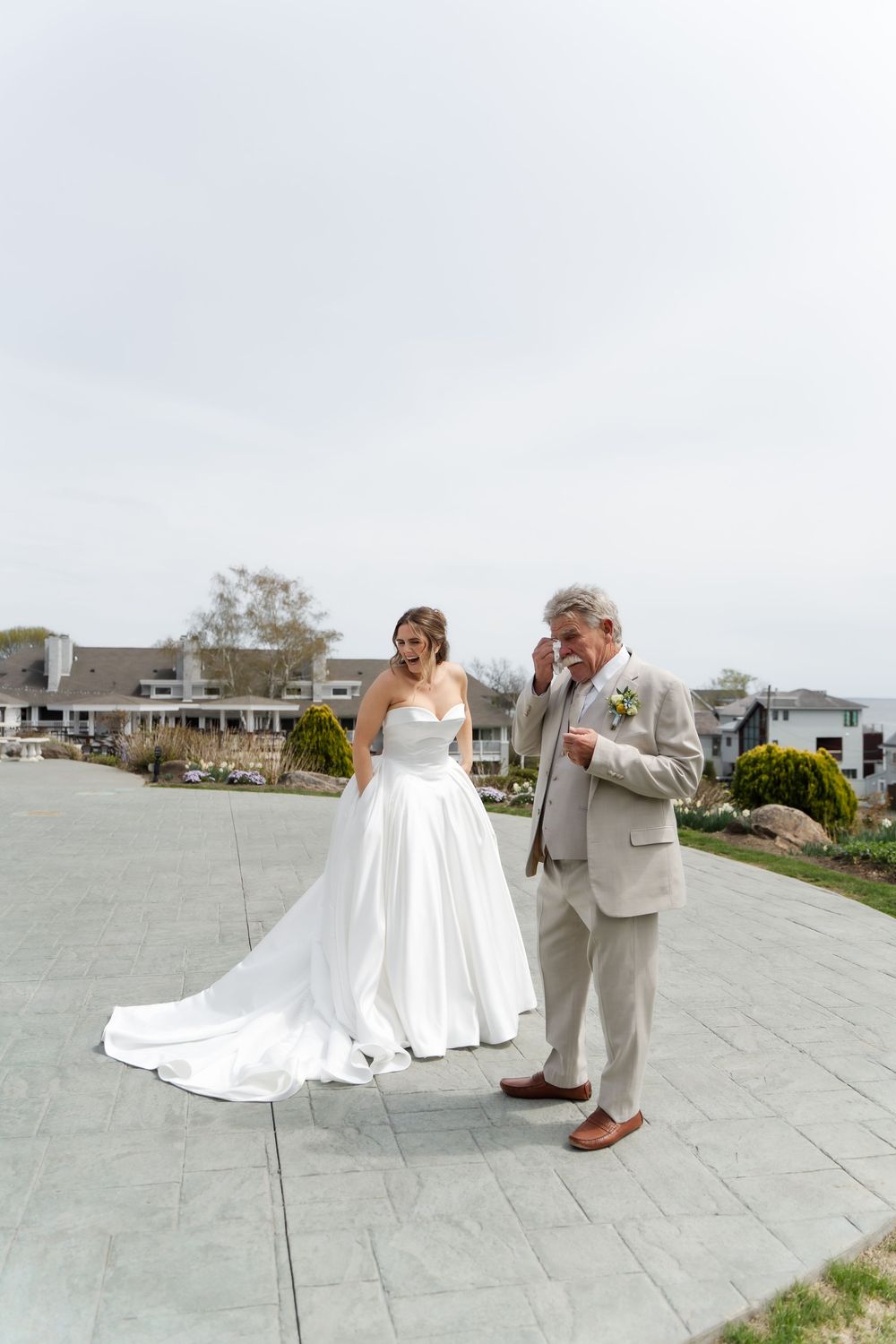Emotional father sees bride daughter in wedding dress for first look on outdoor patio.