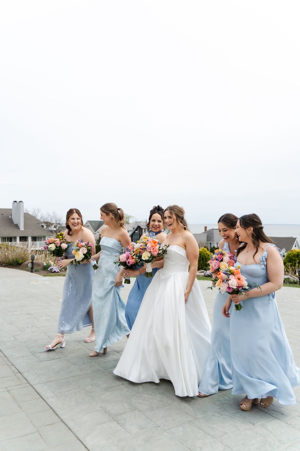 Bride in white gown walks with four bridesmaids in light blue dresses holding colorful bouquets.
