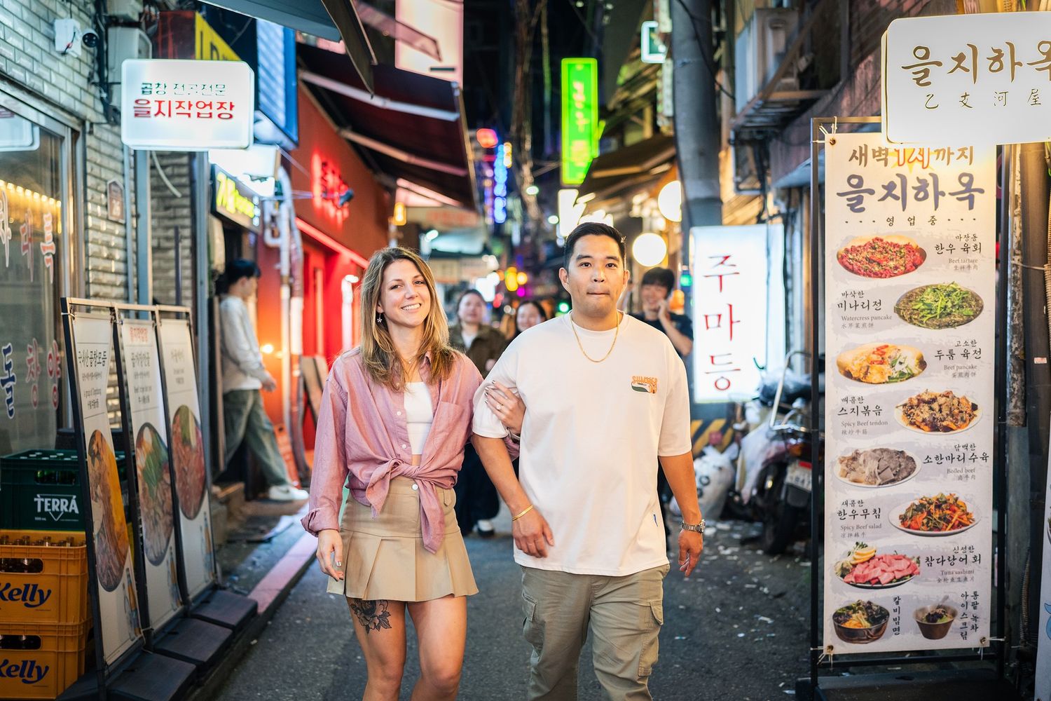 Narrow alley in South Korea lined with illuminated restaurant signs and storefronts at night.