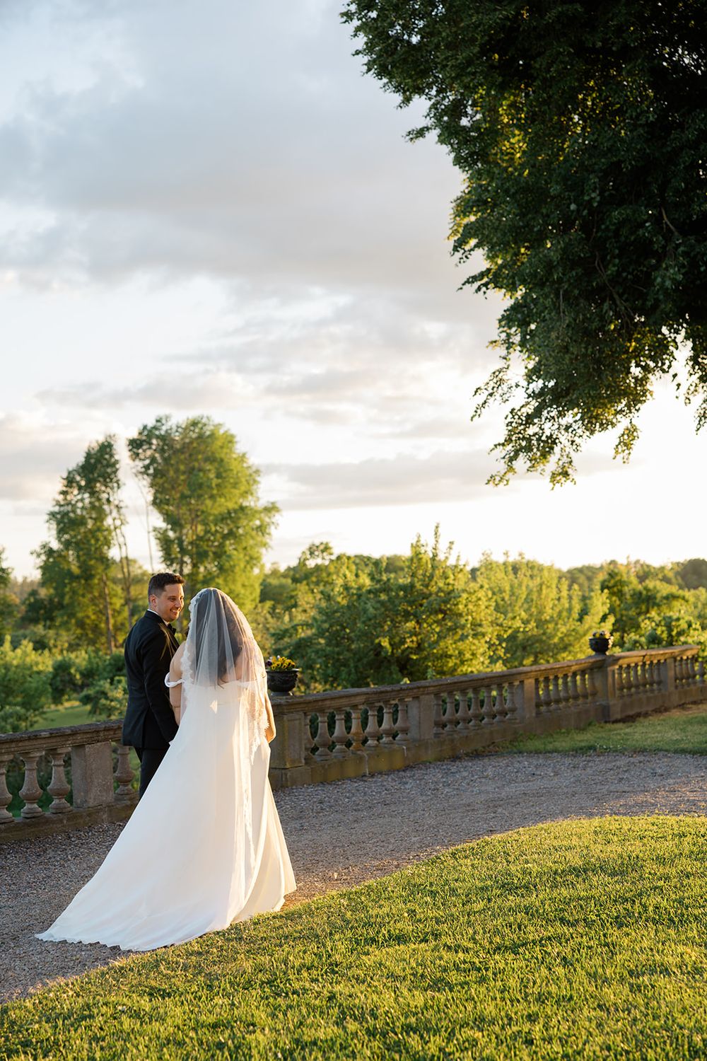 Bride and groom share a romantic moment at golden hour on a garden terrace with lush green trees. Bröllop Hedenlunda Slott
