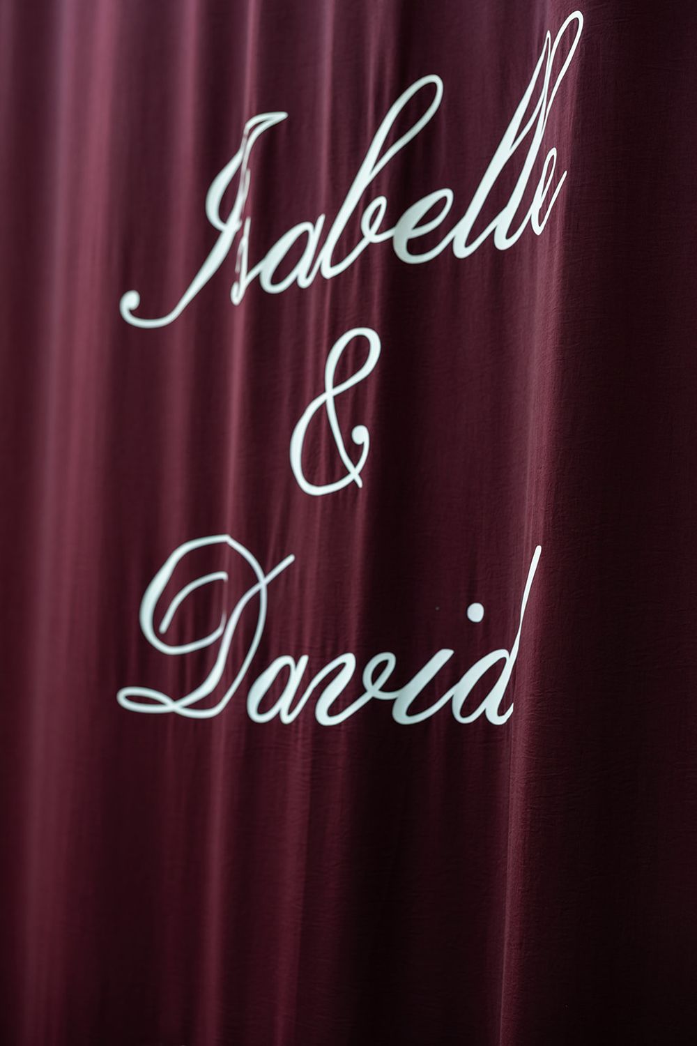 Elegant dark red curtain with silver cursive script reading Isabelle and David for a wedding event.