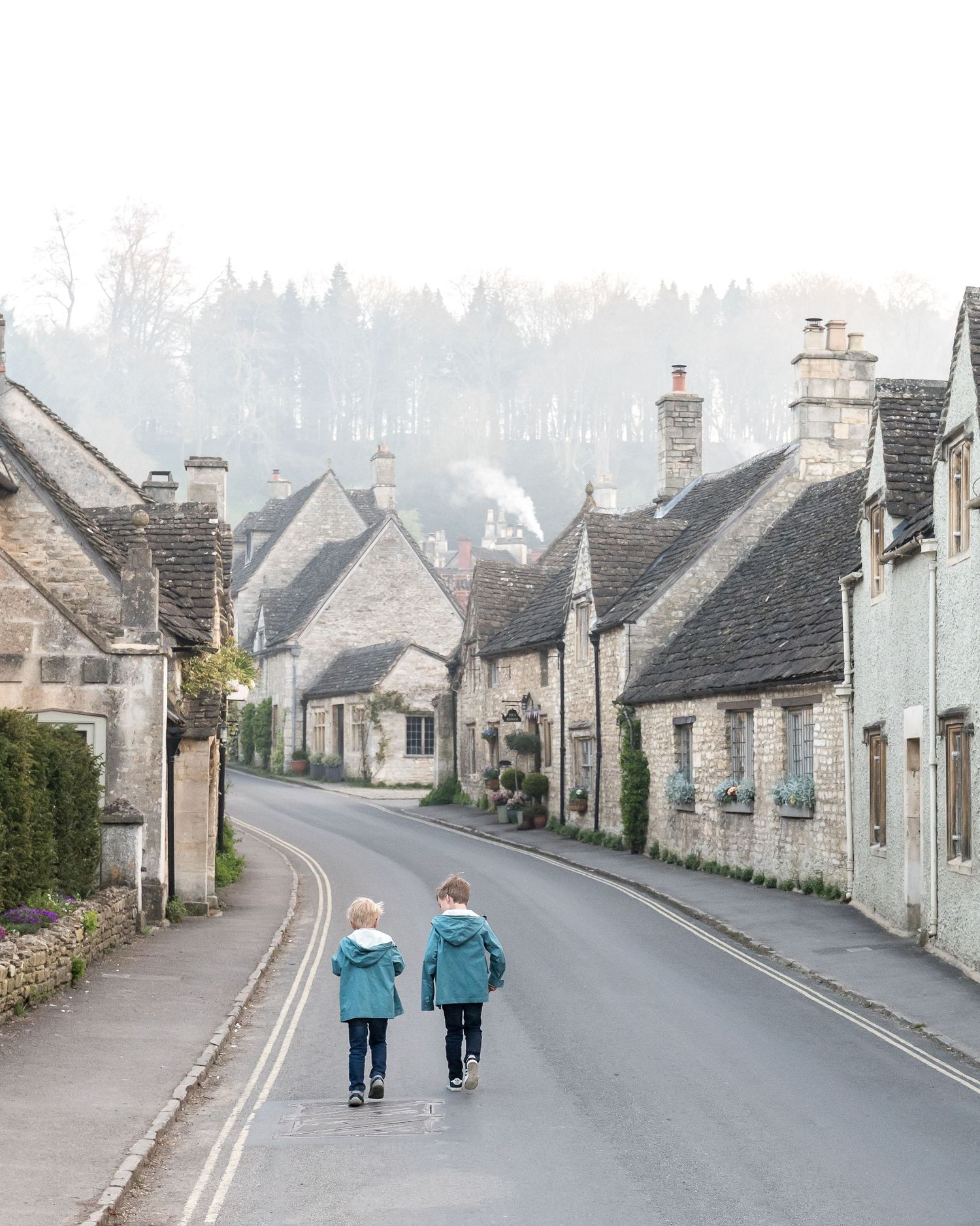 Two people walk down a quaint village street lined with traditional stone cottages in the English countryside.