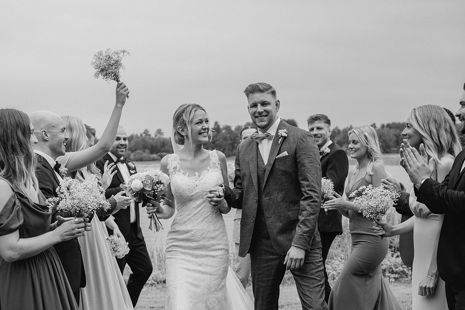 Bride and groom walk through cheering wedding guests in black and white photo.