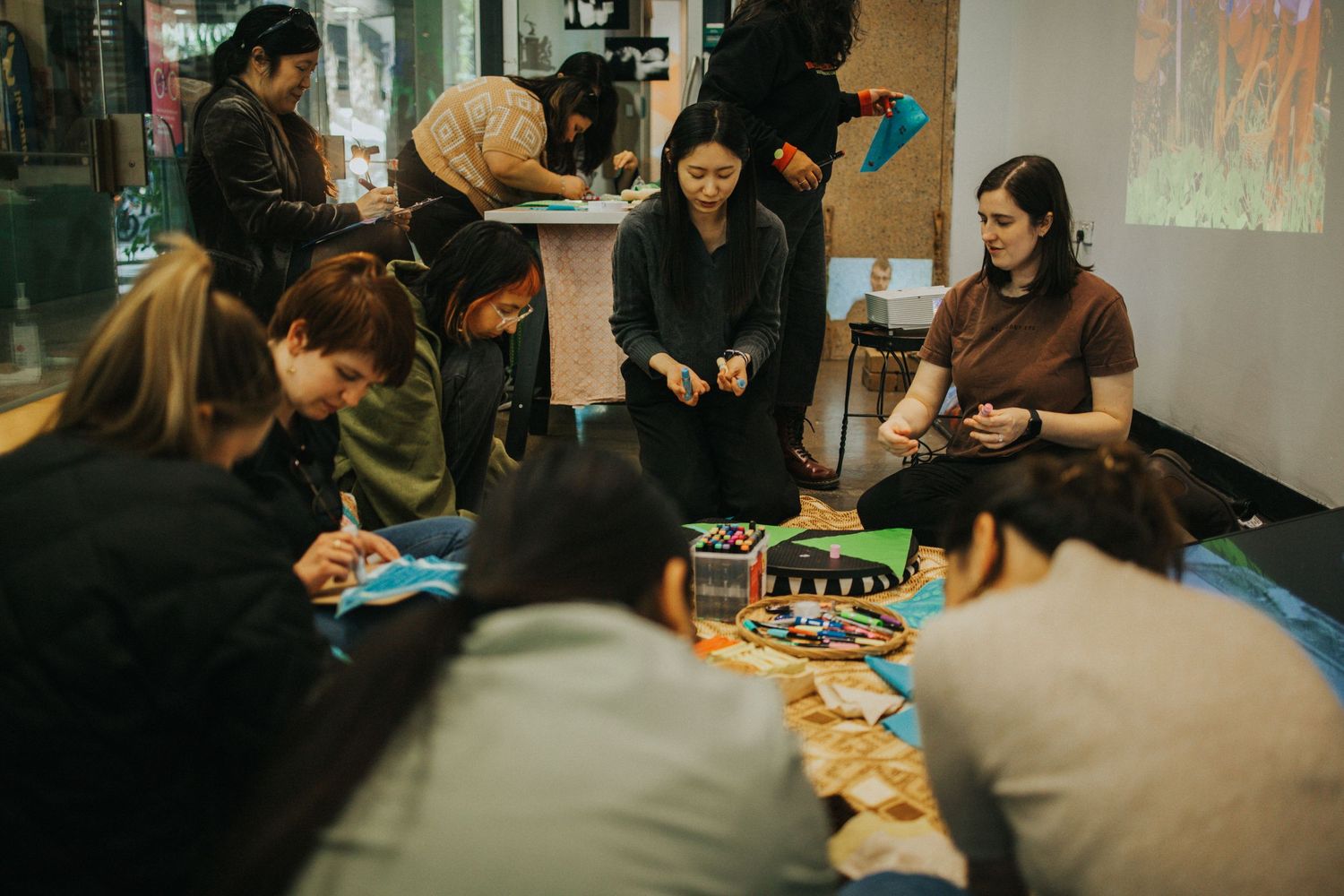 Group of people engaged in a creative workshop activity on the floor of a gallery space.