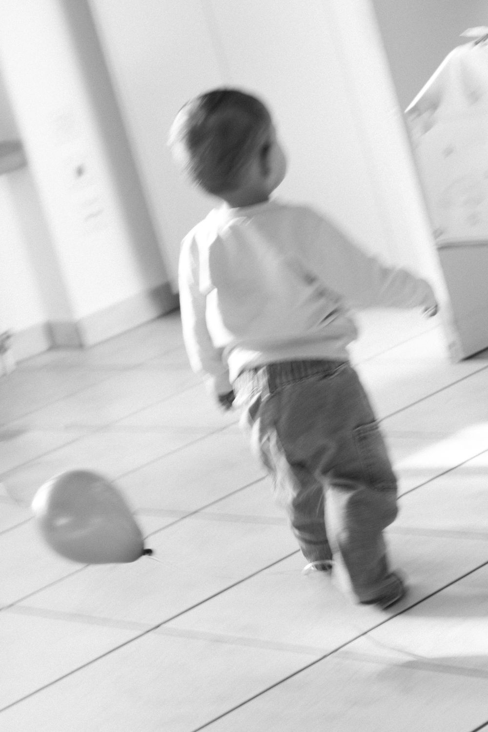 A motion-blurred image of a child running with a balloon on a light floor.