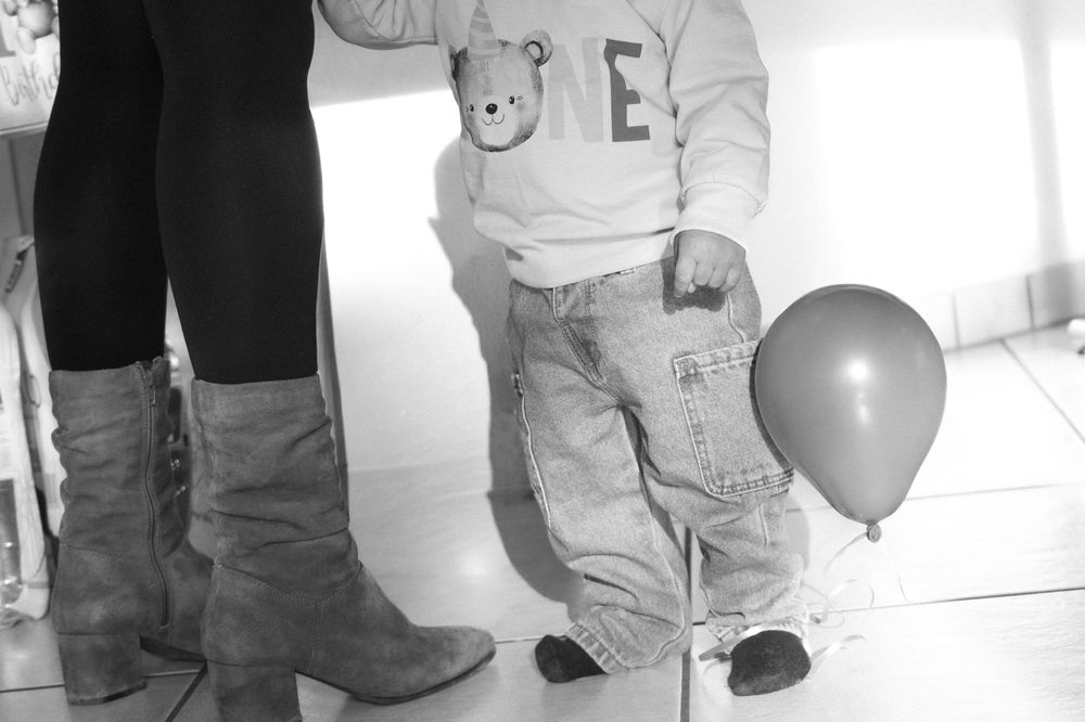 A black and white photo showing boots and small feet with a balloon.