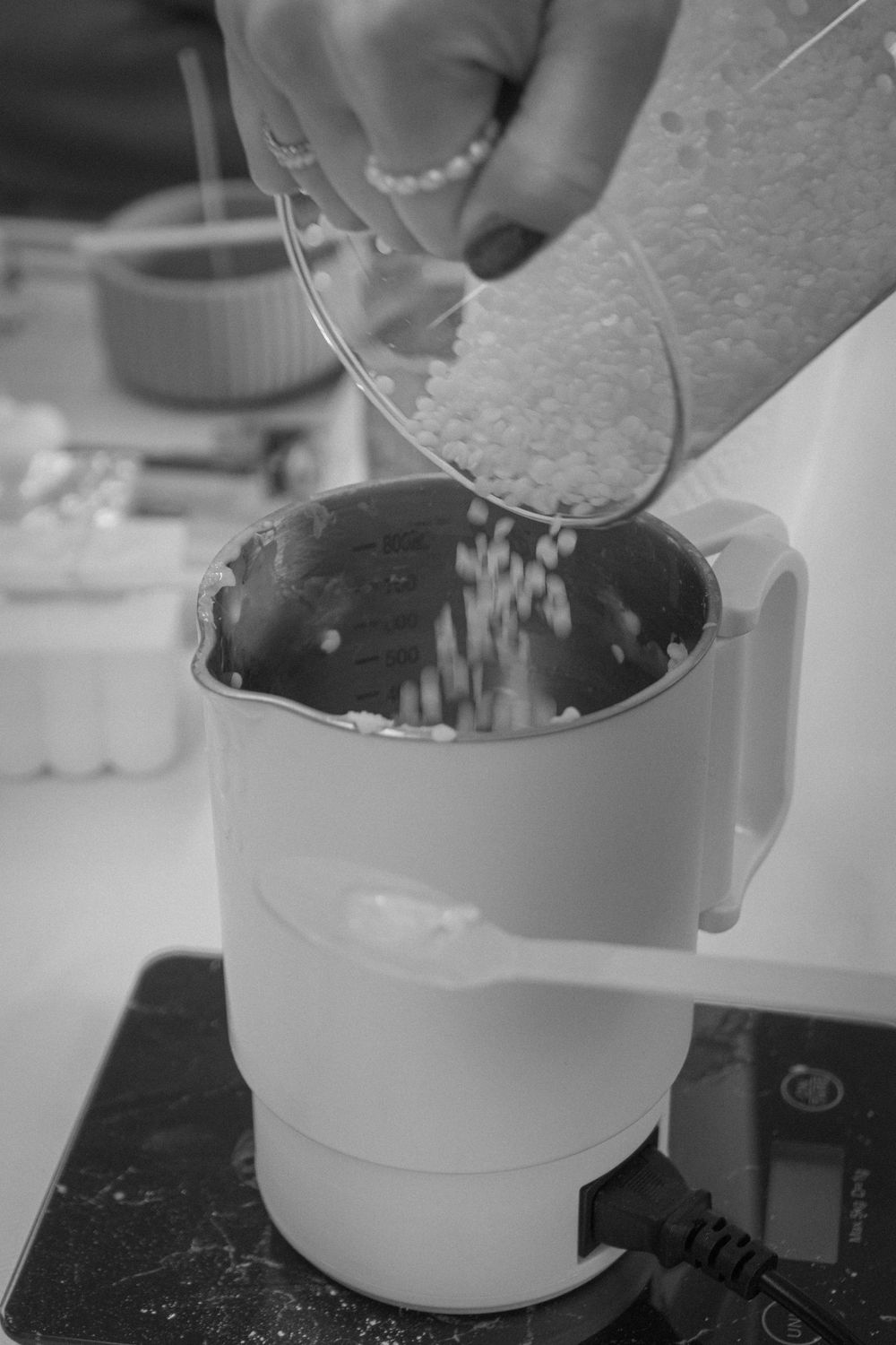 Hands pouring white rice into a measuring jug on a digital kitchen scale in black and white.
