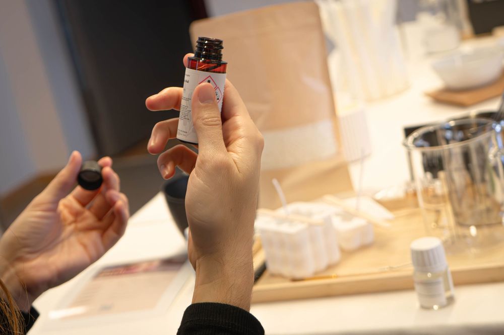 Hands holding a small essential oil bottle with cap removed at a fragrance workshop table.