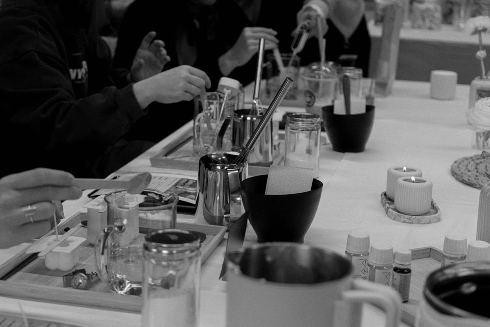 Black and white photo of a busy bar setup with cocktail tools, glasses, and bottles on a white counter.