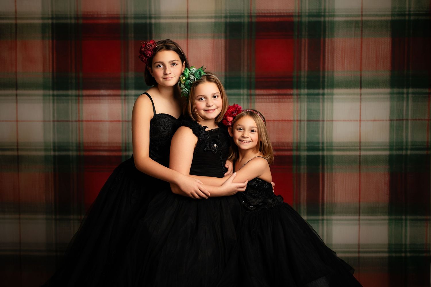 Two people wearing black dresses pose together in front of a plaid backdrop for a holiday portrait session.
