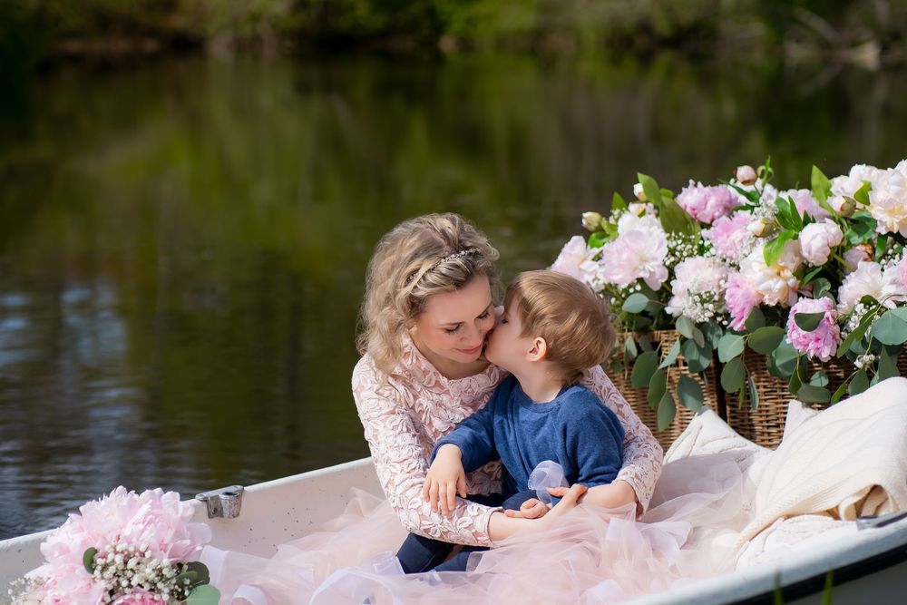 Two people share an intimate moment in a flower-adorned boat surrounded by tranquil waters and lush greenery.