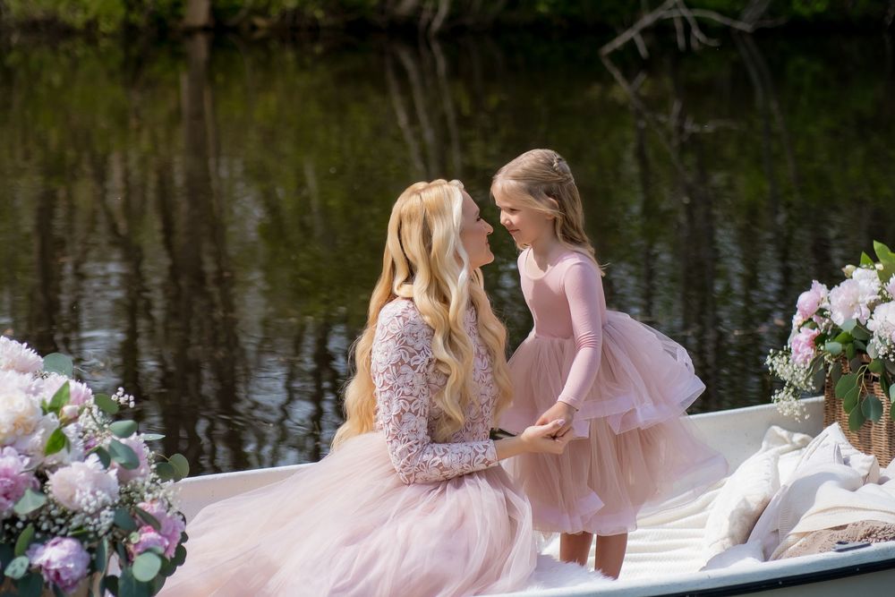 Children in pink dresses sit along a dock by a lake during a dreamy outdoor photo session.