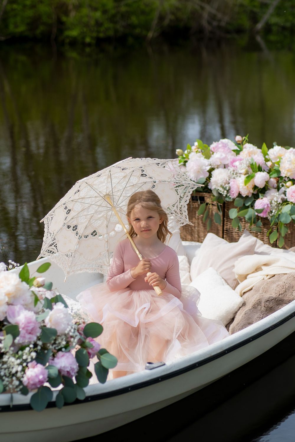 A small boat decorated with pink flowers and parasols floats serenely on dark water.