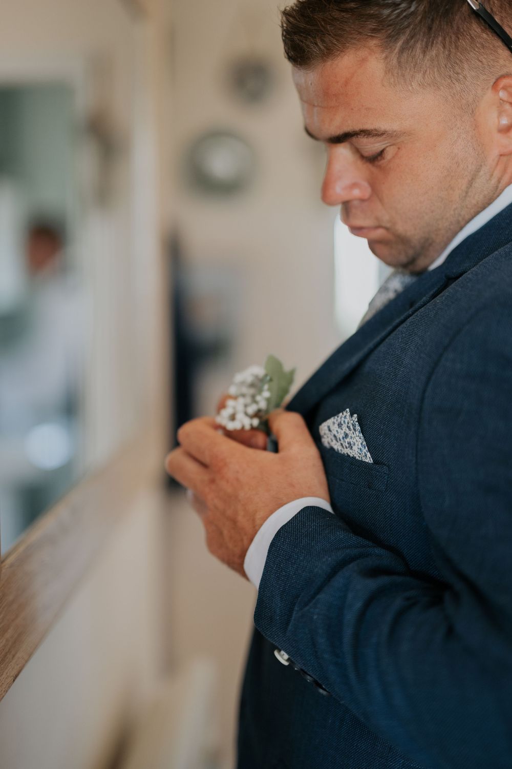 Groom in a navy suit pinning a white floral boutonniere to his lapel before the wedding ceremony.