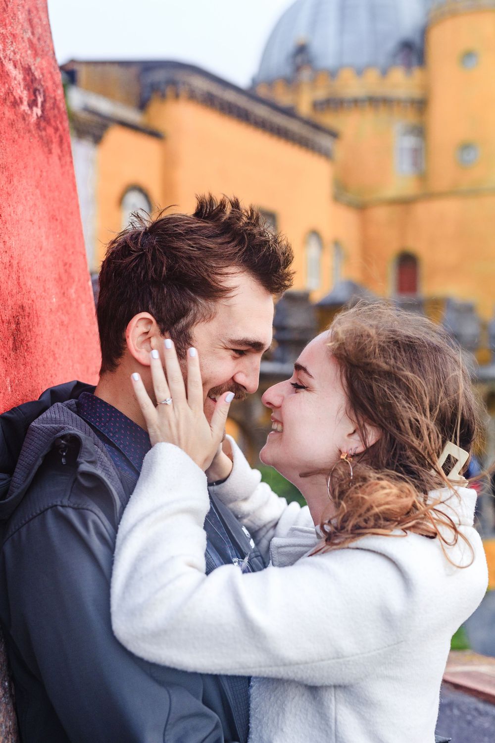 A romantic moment shared between a couple near a yellow castle-like building on a bright sunny day.