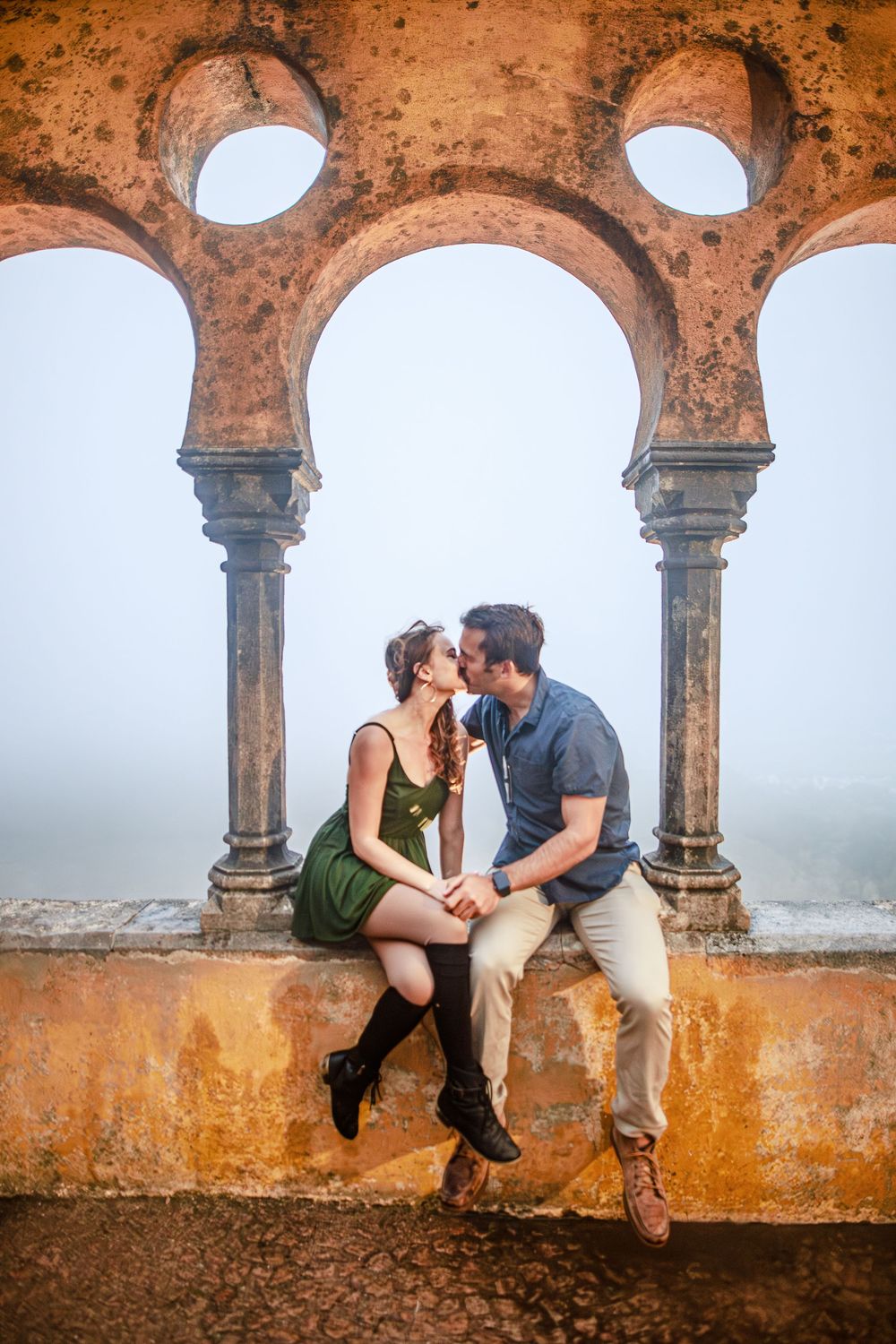 A romantic moment captured between a couple sitting beneath ornate Moorish arches at golden hour in Portugal.