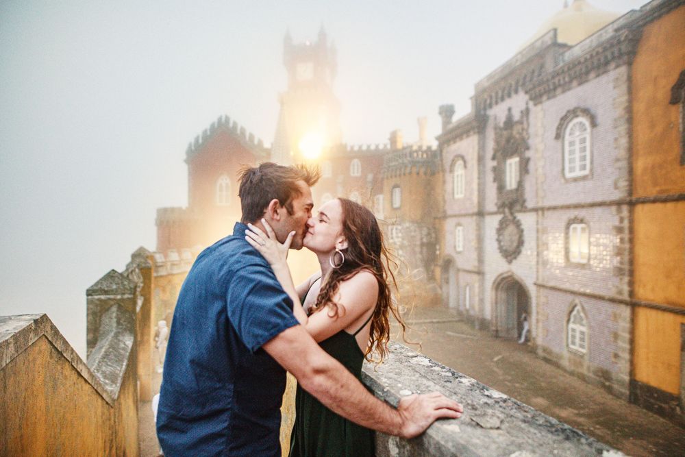 Romantic couple embraces in early morning fog at ancient stone street, golden sunrise illuminating the cobblestones.