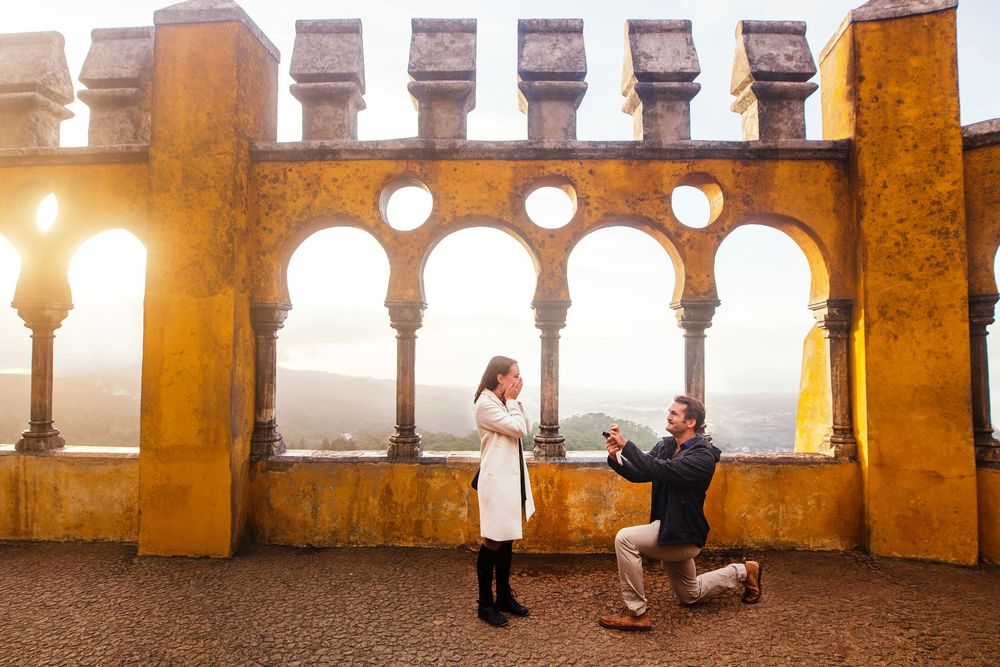 A sunset engagement scene unfolds on a castle balcony with arched columns and glowing warm light.