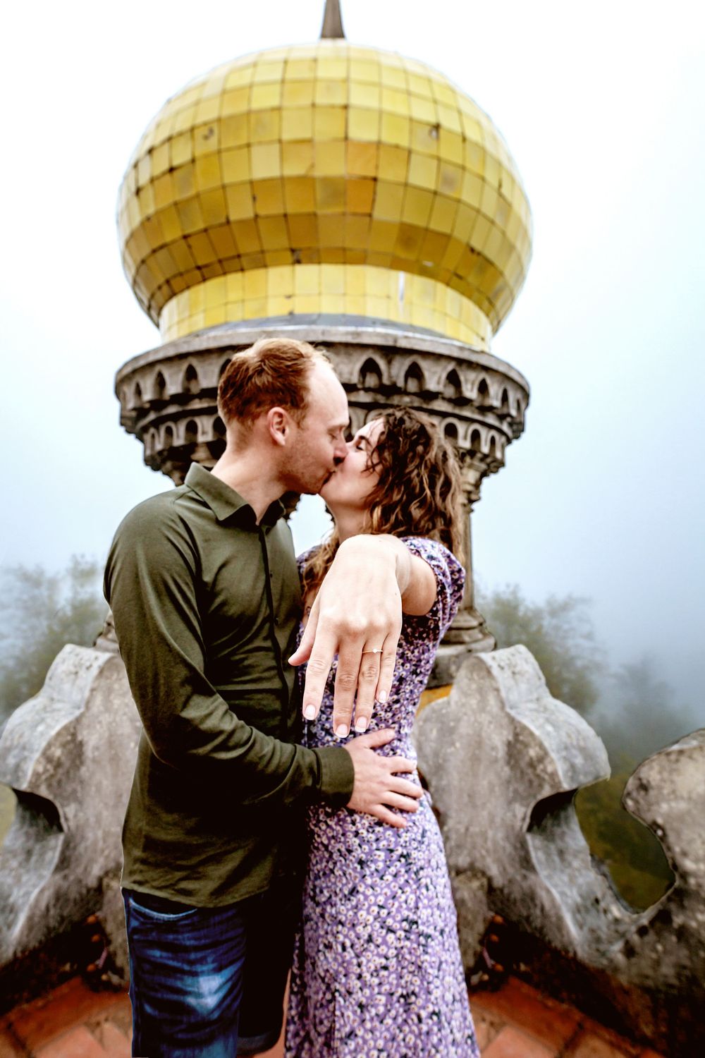 Romantic couple sharing a kiss beneath a golden domed architectural feature covered in delicate mosaic tiles.